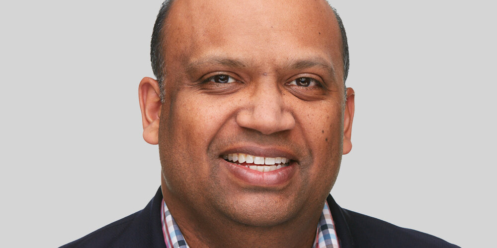 David Duff, a smiling man with short hair, wearing a dark blazer over a checkered shirt, poses against a plain light gray background.