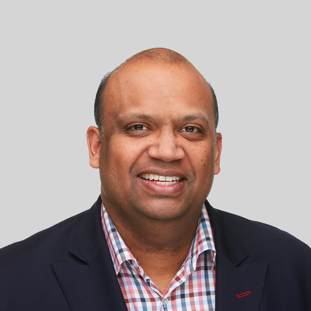 David Duff, a smiling man with short hair, wearing a dark blazer over a checkered shirt, poses against a plain light gray background.