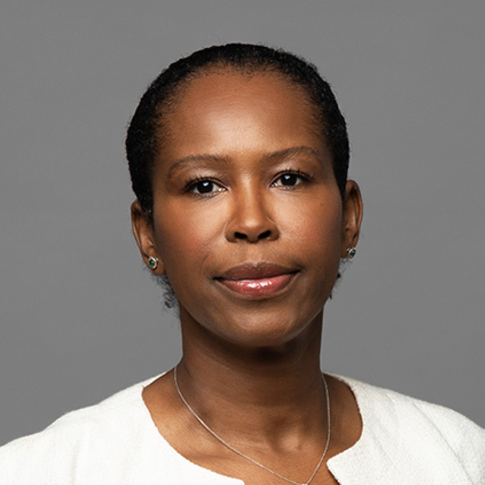 A woman with short black hair, wearing a white top, small stud earrings, and a thin necklace, poses against a plain gray background with a neutral expression—captured in the minimalist style of David Duff.